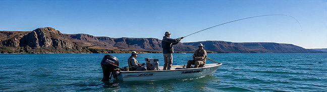 Four anglers casting from a boat on a bright turquoise Patagonian lake
